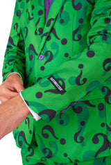 A person dressed in The Riddler suit, a vibrant green ensemble with a pattern of large black question marks. One hand is adjusting the cuff of the jacket, which features a label from Suitmeister. The suit is complemented by a purple shirt and tie.