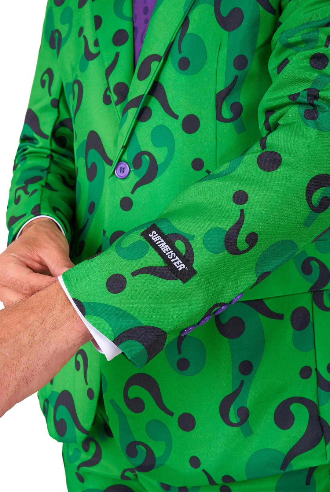 A person dressed in The Riddler suit, a vibrant green ensemble with a pattern of large black question marks. One hand is adjusting the cuff of the jacket, which features a label from Suitmeister. The suit is complemented by a purple shirt and tie.