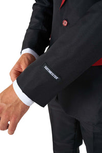 A person adjusting the sleeve of a black Harry Potter Gryffindor™ Suit by Suitmeister, with the brand name embroidered near the cuff. The suit features red accents, and the person's hand is visible as they hold the jacket sleeve.