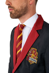 A man dressed in a Suitmeister Harry Potter Gryffindor™ Suit, featuring a dark blazer adorned with a red lapel and the Gryffindor crest. He completes his look with a white shirt and a red and yellow striped tie, all set against a plain white background.