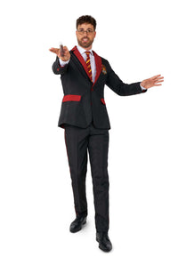 A man dressed in the Suitmeister Harry Potter Gryffindor™ Suit, featuring a black design with red accents and a striped tie, holds a wand in one hand while standing with one foot forward as if casting a spell. The scene is set against a plain white background.