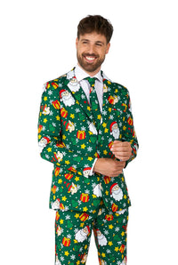 A man dressed in the Suitmeister Santa Elves Green - Christmas suit, which features festive prints of Santa, snowflakes, and gifts. He is smiling while adjusting his jacket with one hand.