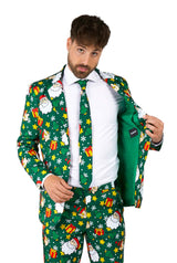 A man is sporting the Suitmeister Santa Elves Green Christmas suit, featuring lively patterns of Santa Claus, gifts, and snowflakes. He's paired it with a white shirt and matching tie and is revealing the plain green lining by opening his jacket.