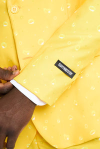 Close-up of a person adjusting the sleeve of a Premium Beer Yellow suit, characterized by its playful bubble pattern. The sleeve prominently displays the Suitmeister label.