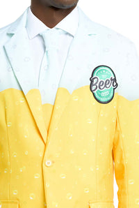 A person is wearing the "Premium Beer Yellow" suit by Suitmeister, designed to resemble a glass of beer. The jacket features a gradient from white to yellow with bubble graphics, and has a patch displaying the word "Beer." The shirt and tie are in light colors.