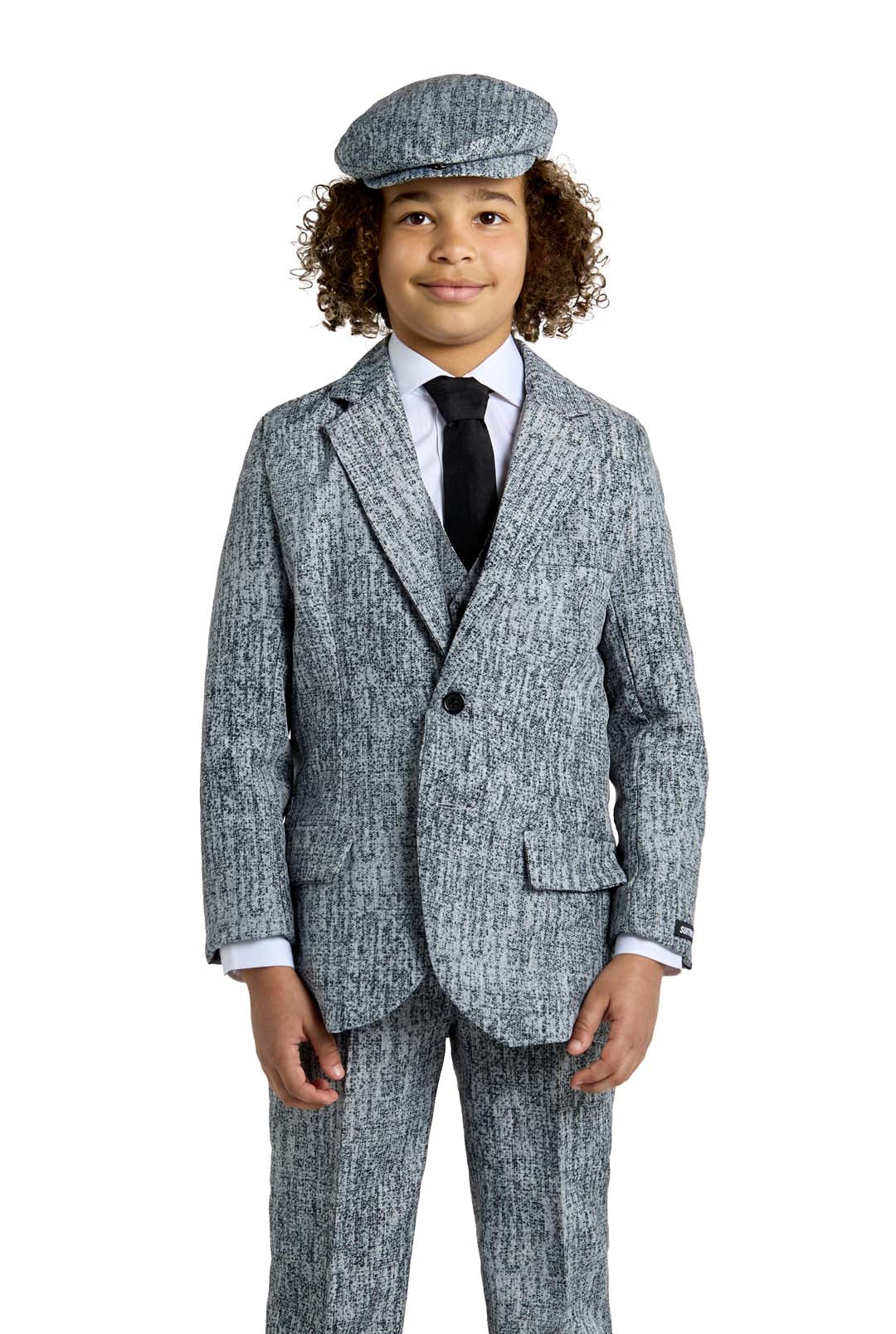 A young boy with curly hair is dressed in the 20's Gangster Grey Halloween suit from Suitmeister, complete with a matching flat cap, white shirt, and black tie. He stands with a neutral expression against a plain white background.