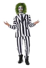 A person wearing the Suitmeister Beetlejuice costume stands with arms outstretched, smiling mischievously. They have green, messy hair and pale face makeup with dark eye circles, resembling a classic movie character.