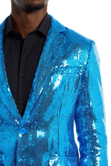 A person is dressed in a Suitmeister Sequins Blue Blazer over a black shirt. The shiny blazer reflects light in various shades of blue. Only the upper torso can be seen.