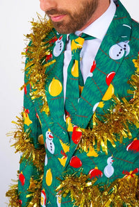 A man is wearing the Suitmeister's "Christmas Deco Green" suit, featuring festive designs of snowmen, balloons, and gold tinsel. The ensemble includes a coordinating tie and is set against a simple background.