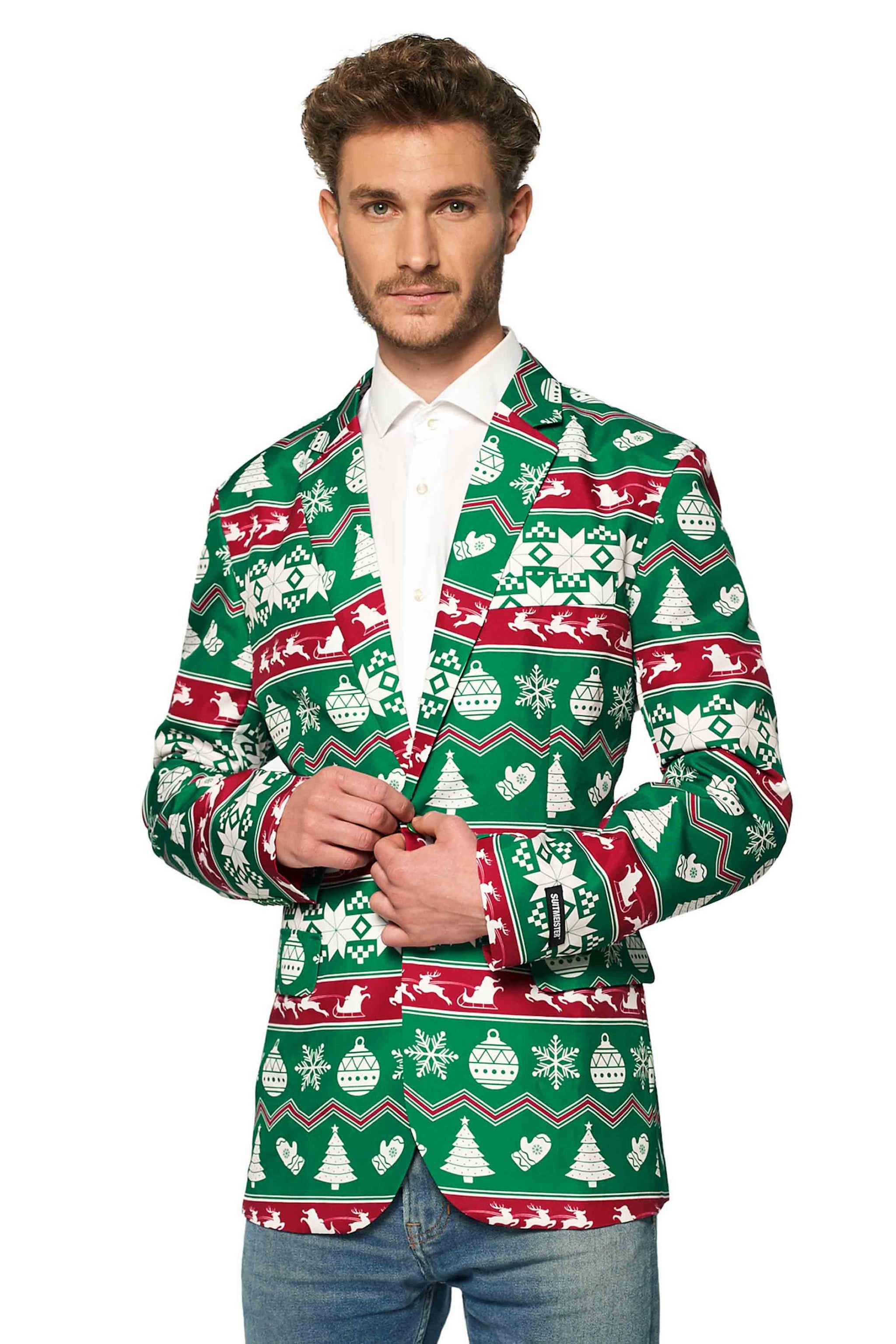 A man wearing a Suitmeister Christmas Green Nordic Jacket, featuring festive red and white holiday patterns such as snowflakes, trees, and ornaments, layered over a white shirt and jeans. He is standing against a plain white background.