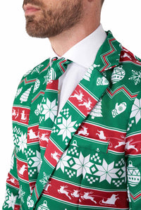 A man dressed in the Suitmeister Christmas Green Nordic ensemble, featuring a festive green and red suit adorned with snowflake, reindeer, and Christmas tree patterns, complemented by a matching tie and a white shirt underneath.