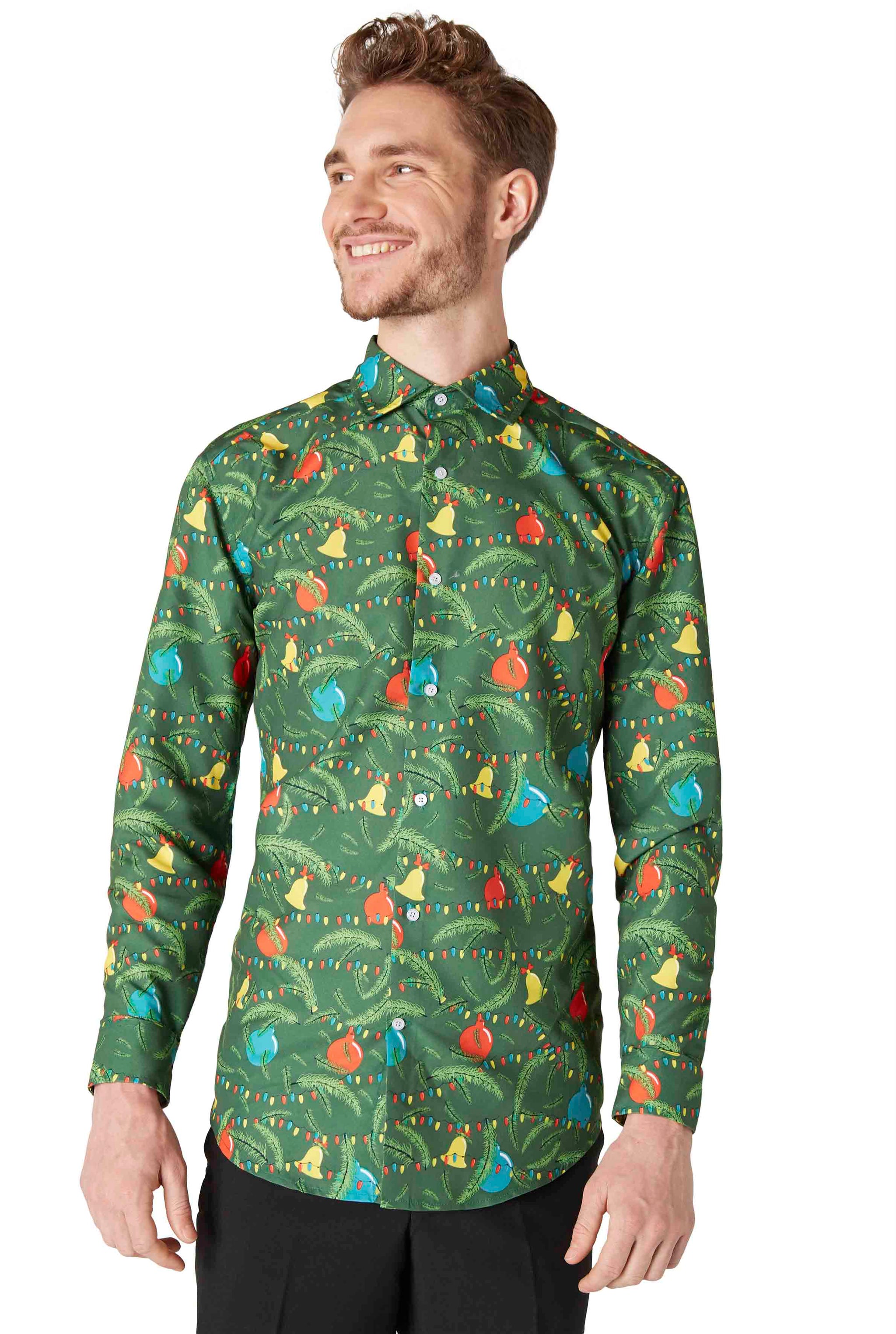 A smiling person wearing the Suitmeister Christmas Green Tree Shirt, which features colorful and playful patterns of birds, leaves, and ornaments, paired with black pants. The background is plain white.