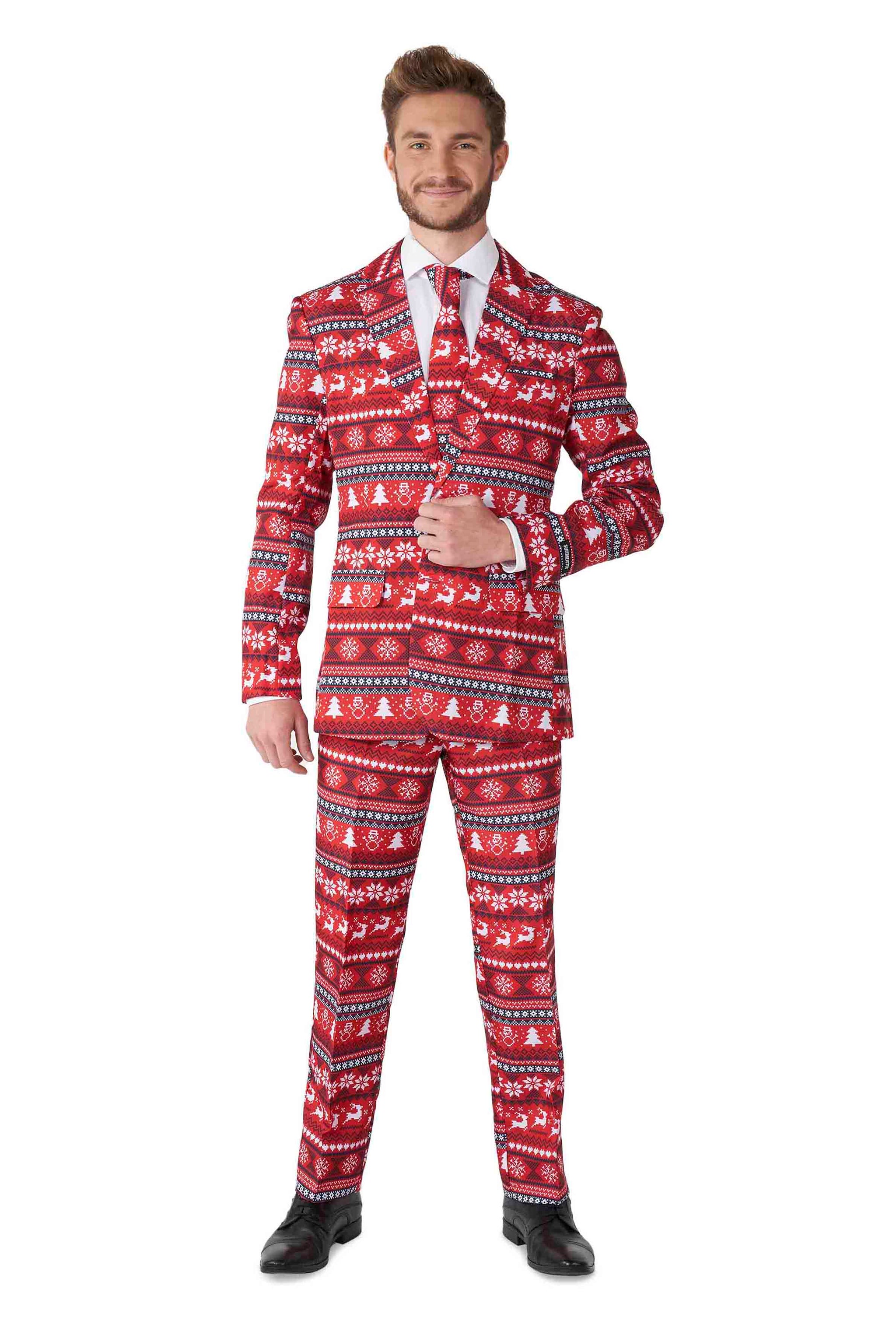 A man dressed in the Suitmeister Nordic Pixel Red - Christmas suit, featuring a festive red design adorned with white holiday patterns like snowflakes and reindeer. He pairs it with a crisp white shirt and matching tie, standing confidently with one hand on his lapel, smiling warmly.