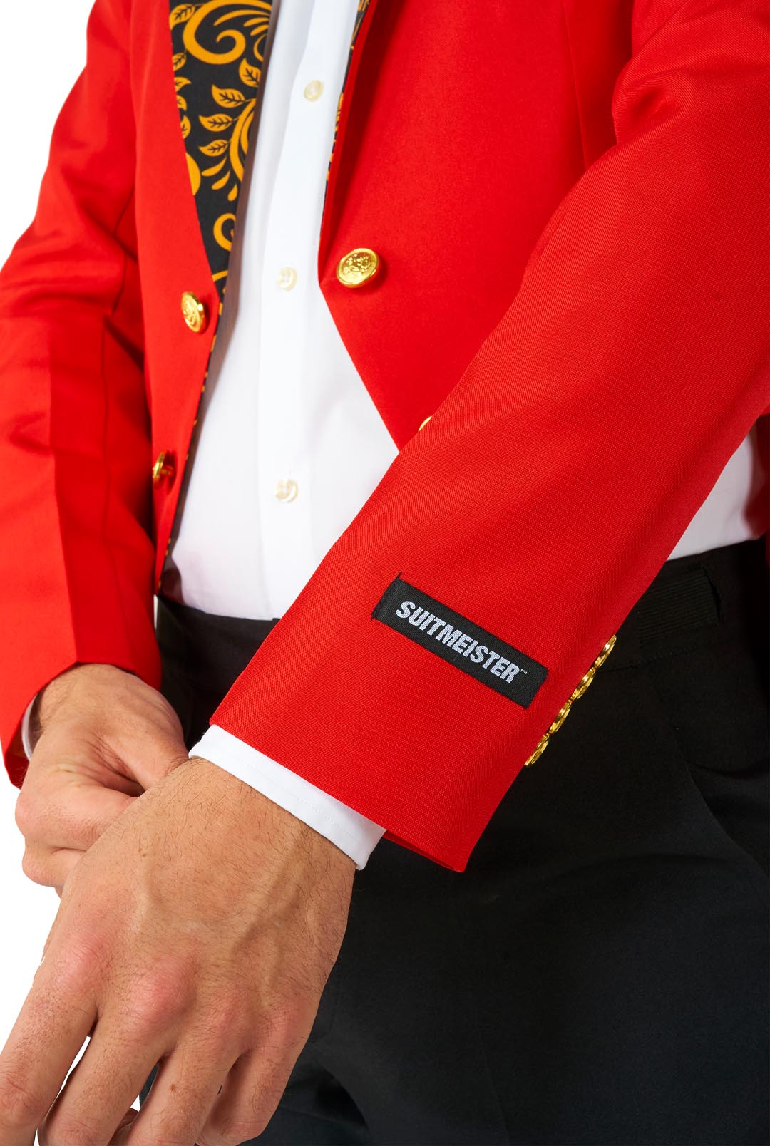 A person wearing the vibrant Circus Tailcoat Suit Red with gold accents, paired with a black and gold patterned tie. The sleeve features a label from the brand Suitmeister, and they are adjusting the cuff. The background is plain white.