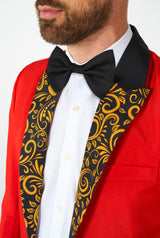 A man is dressed in the Suitmeister Circus Tailcoat Suit Red, featuring a red suit jacket with an intricate black and gold ornate patterned lapel. He pairs it with a white shirt and a black bow tie, emphasizing his upper body's detailed design.