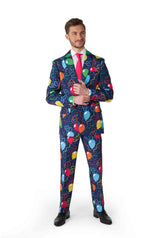 A man confidently stands in a vibrant Suitmeister ensemble adorned with the Confetti Balloons Navy pattern. He pairs it with a white shirt, a bright pink tie, and black shoes, set against a plain white background.