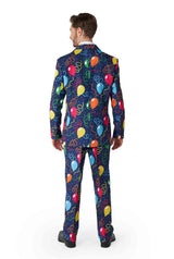 Wearing the Suitmeister Confetti Balloons Navy suit, a person stands facing away with a playful and colorful balloon pattern featuring bright hues of red, blue, yellow, and orange. The festive design is set against a plain white background.