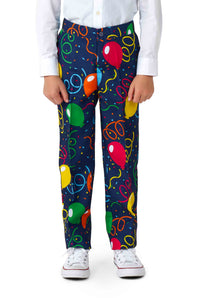 A child wearing colorful Confetti Balloons Navy pants from Suitmeister stands with hands by their sides. They are also wearing a white shirt and white sneakers with red details. The background is plain and unobtrusive.