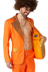 A man confidently smiles in a Suitmeister "Disco Suit Orange" adorned with sequin details on the collar and pocket, which opens to reveal a coordinating sequin trim inside. Sporting curly hair, sunglasses, and a gold chain, he exudes style and charm.