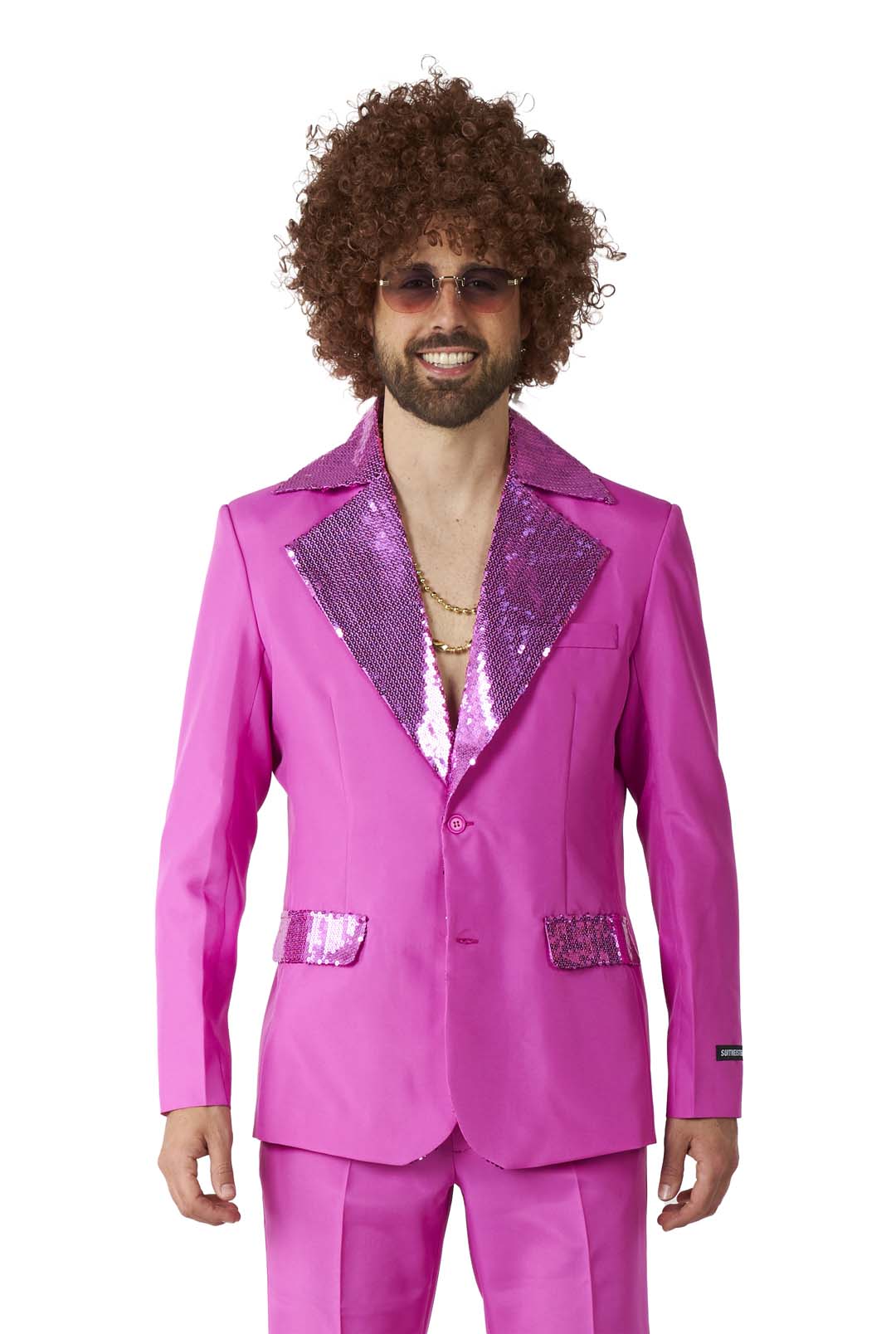 A person wearing the Disco Suit Pink by Suitmeister, featuring a bright pink disco-style suit with sequined lapels and pocket accents, complemented by sunglasses and a curly wig. The suit jacket is paired with a partially unbuttoned shirt that reveals gold necklaces.