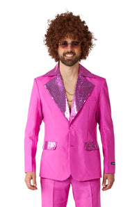 A person wearing the Disco Suit Pink by Suitmeister, featuring a bright pink disco-style suit with sequined lapels and pocket accents, complemented by sunglasses and a curly wig. The suit jacket is paired with a partially unbuttoned shirt that reveals gold necklaces.