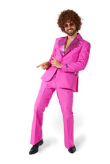 A person with curly hair is wearing a Disco Suit Pink by Suitmeister, complete with shiny lapels, along with black shoes and sunglasses, striking a playful pose against a white background.