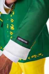 A person is dressed in Suitmeister's Elf™ suit, which boasts a green fabric adorned with festive yellow patterns including icons like snowmen and candy canes. The white cuff displays the Suitmeister brand label, and the sleeve stops just above yellow pants.