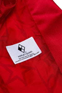 A close-up of a red fabric showcases a white clothing label featuring a diamond pattern with the text "Harley Quinn™" by Suitmeister. The label states that the design draws inspiration from characters and elements of DC Comics.