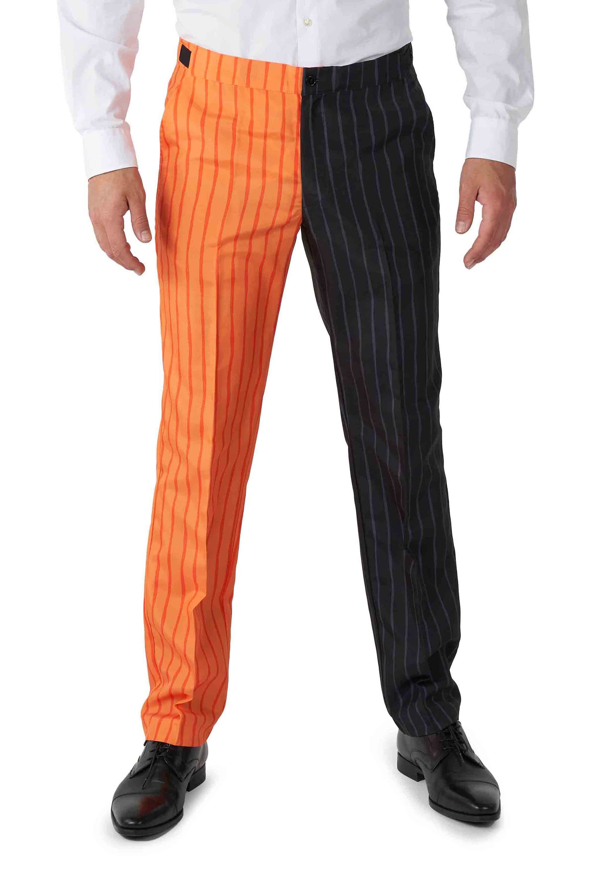 A person dressed in the Jack-O Pinstripe Black Halloween suit by Suitmeister, featuring pants with one leg in orange and black stripes and the other in black and white stripes, along with a crisp white shirt and sleek black shoes.