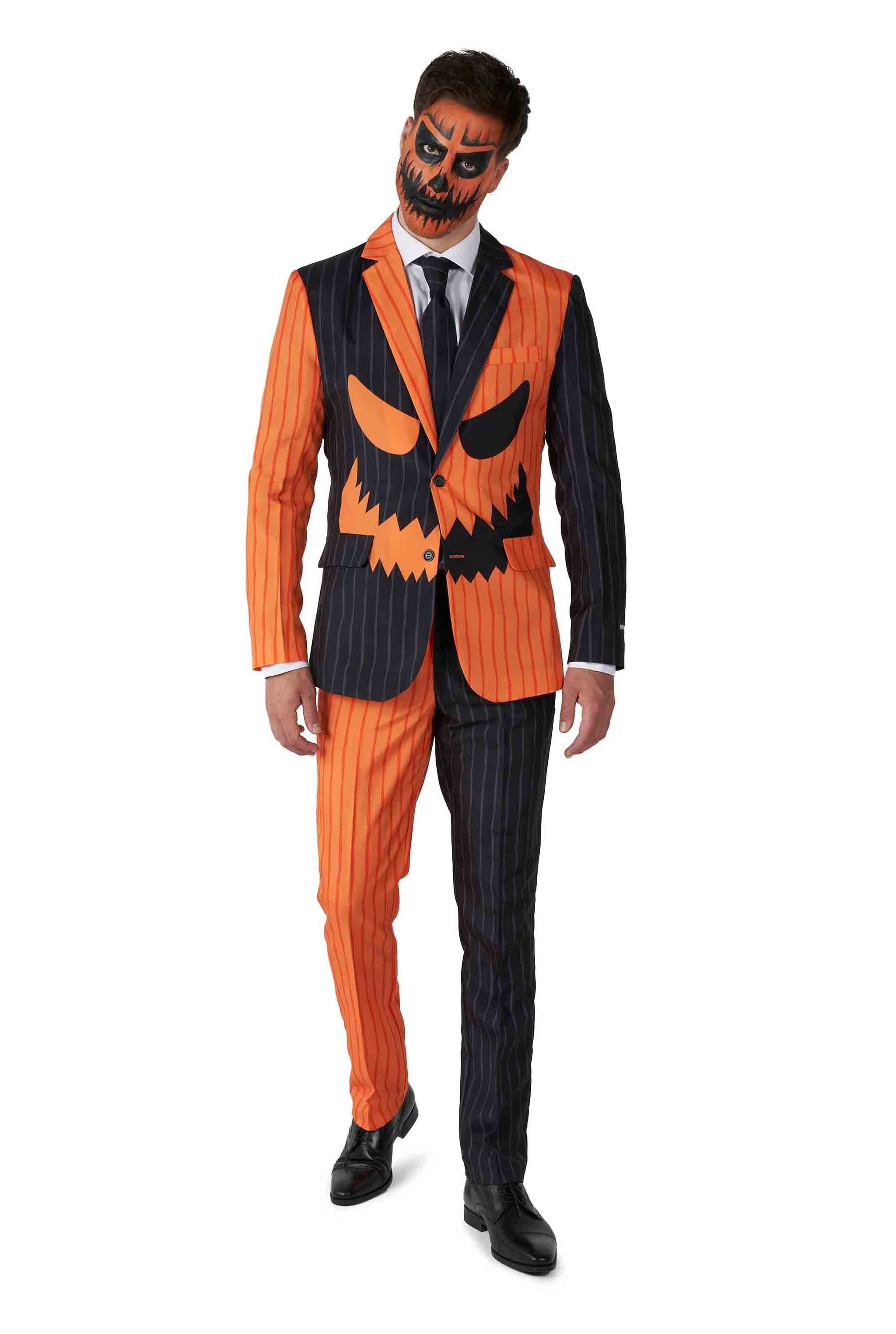 A person is dressed in the Suitmeister Jack-O Pinstripe Black suit, featuring a half-orange, half-black pinstriped design with a jack-o-lantern face motif on the jacket. Their face is painted to match the pumpkin design, and they complete the ensemble with black shoes and a black tie.