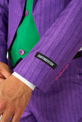 Close-up of a person wearing the Joker™ Tailcoat Suit Purple, featuring a green shirt underneath. The sleeve of the suit prominently displays the Suitmeister label, and the outfit is completed with distinctive purple buttons. The image focuses on the sleeve as the person adjusts their jacket.