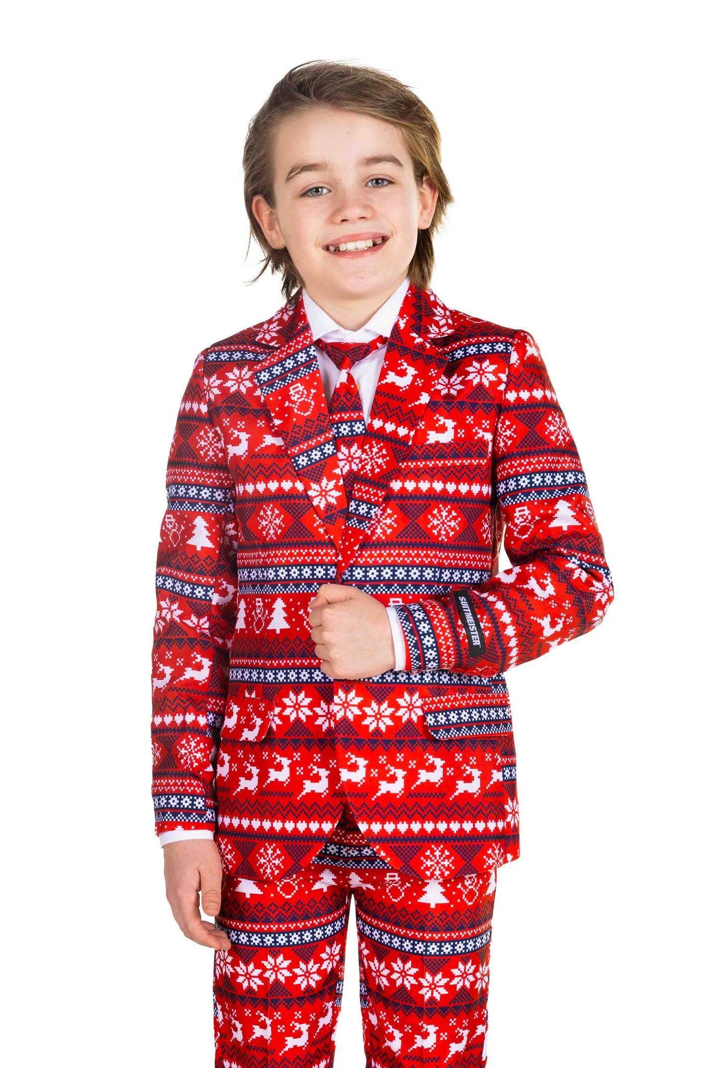 A smiling child dressed in the Suitmeister Nordic Pixel Red Christmas suit, showcasing a festive pattern of reindeer, snowflakes, and trees in red, white, and black. They complete the outfit with a crisp white shirt and a vibrant red tie.