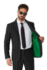 A man in a Suitmeister Oversized Pinstripe Black suit, paired with a matching tie and white shirt, holds open his jacket to reveal its vivid green lining. He sports sunglasses and exudes confidence.