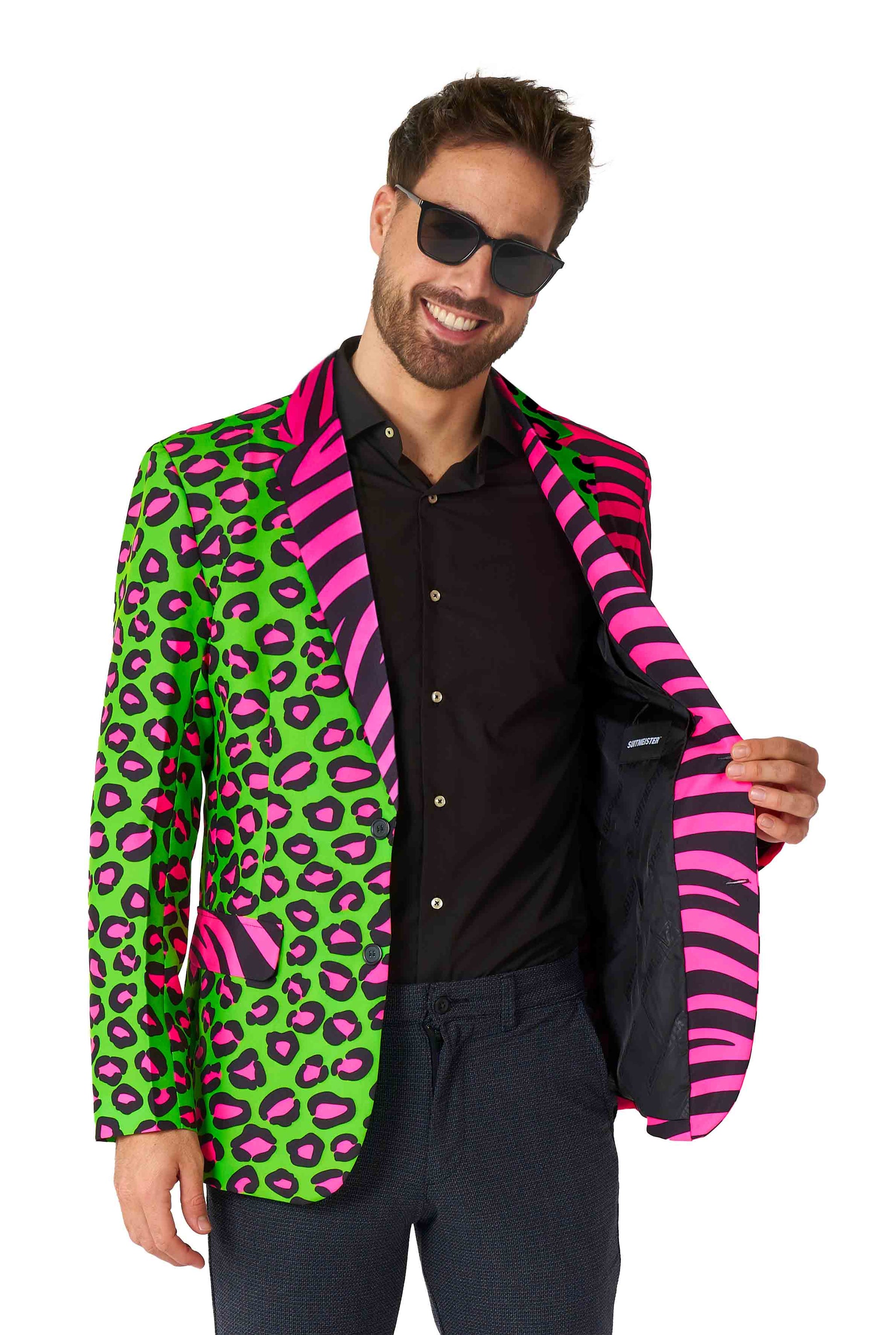 A man in sunglasses smiles while wearing the Suitmeister Party Animal Neon blazer featuring a vibrant green and pink leopard print. He opens the jacket to reveal a striking pink and black zebra-striped lining, perfectly paired with his black shirt and dark pants.