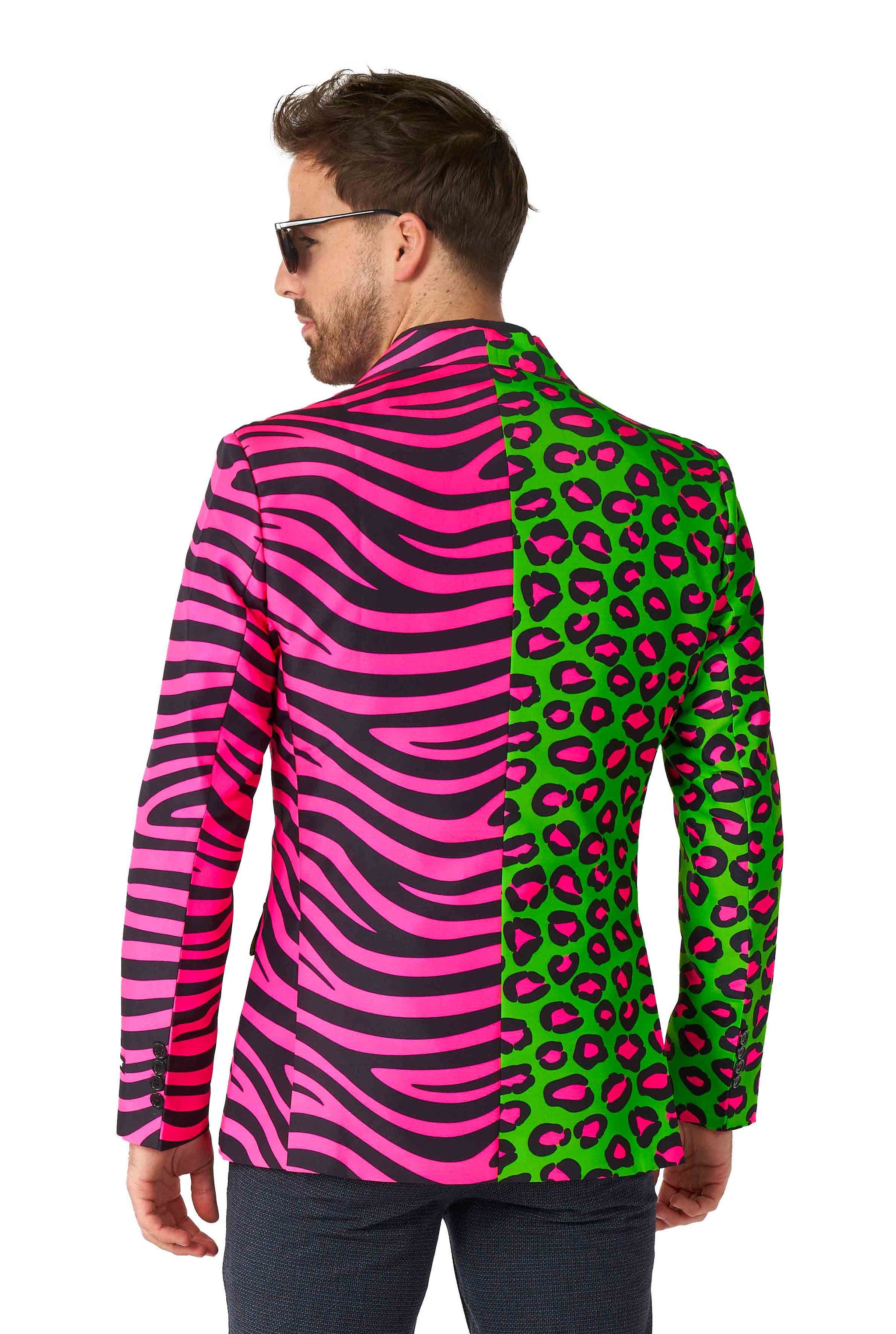 A man dressed in the Suitmeister's Party Animal Neon ensemble, featuring a vibrant mix of mismatched patterns, stands facing away. One side of the suit showcases a pink and black zebra print, while the other side displays a green and pink leopard print. He completes his look with dark pants and sunglasses.