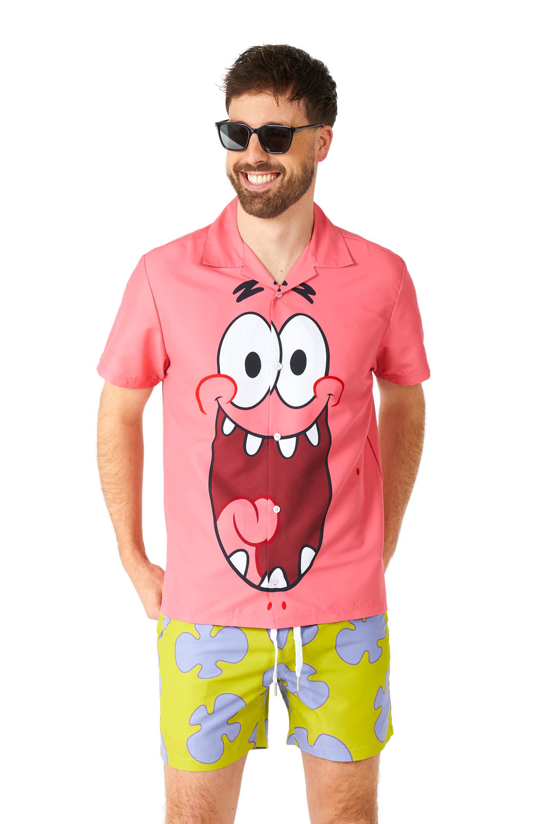 A man dressed in a Suitmeister Patrick costume, featuring sunglasses and a pink shirt adorned with a cartoon face, is smiling. He is also wearing bright green shorts with distinctive purple cloud-like patterns.