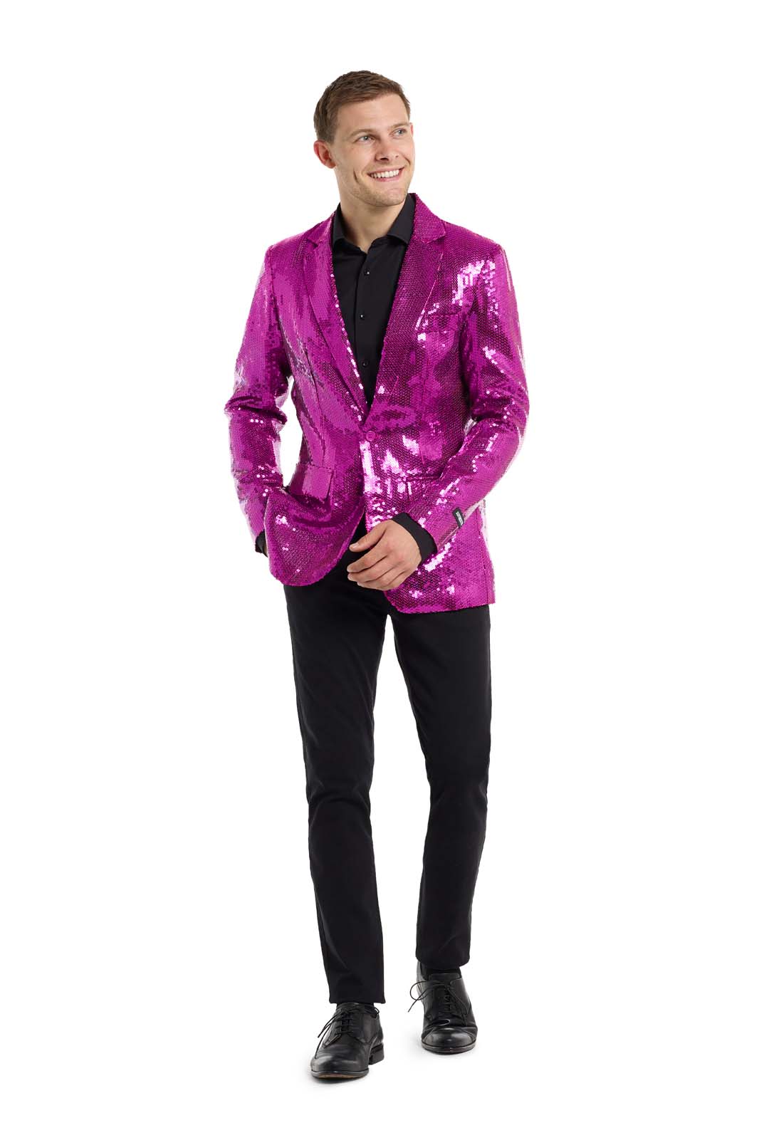 A man wearing a sparkling pink Suitmeister Sequins Blazer over a black shirt and black pants, standing and smiling. He is looking to the side, with his hands relaxed by his sides.