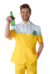 Dressed in the Premium Beer Yellow novelty suit from Suitmeister, a man resembling a frothy-topped beer glass smiles broadly. The suit boasts a fun beer-themed pattern, and he pairs it with a white shirt and tie underneath while holding up a green beer bottle.