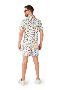 A man with short hair and sunglasses stands facing away, dressed in a Suitmeister Pride Icons White ensemble—a vibrant matching shirt and shorts set with a playful pattern of abstract shapes on a white background. He completes the look with white shoes.