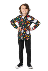 A smiling child stands with hands on hips, dressed in a Suitmeister Santa Elves Black Christmas shirt featuring colorful Santa and gift designs, paired with black pants and black sneakers. The background is white.