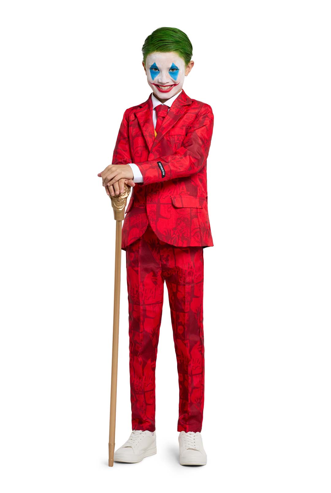 A child dressed in the Scarlet Joker ensemble by Suitmeister, featuring a vibrant red suit adorned with geometric patterns, white face paint accented with blue designs around the eyes, and green hair, stands holding a cane topped with gold. The outfit is completed with white shoes and a red tie.