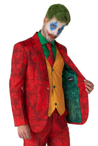 A person wearing the Scarlet Joker™ suit from Suitmeister, featuring a vivid red and orange design with green accents reminiscent of a comic character's style. They have green hair and white face paint adorned with blue and red markings while showcasing the jacket's interior lining.