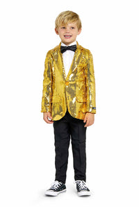 A young boy stands smiling, dressed in a Suitmeister Sequins Gold sequin blazer over a white dress shirt paired with a black bow tie. He completes his outfit with black pants and stylish black-and-white sneakers. His blond hair and cheerful expression add to his charming appearance.