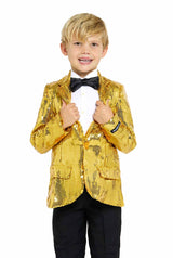 A young boy smiling and looking directly at the camera, wearing the Sequins Gold - Sequin Blazer by Suitmeister paired with a white shirt, black bow tie, and black pants. He is holding the lapels of his jacket.