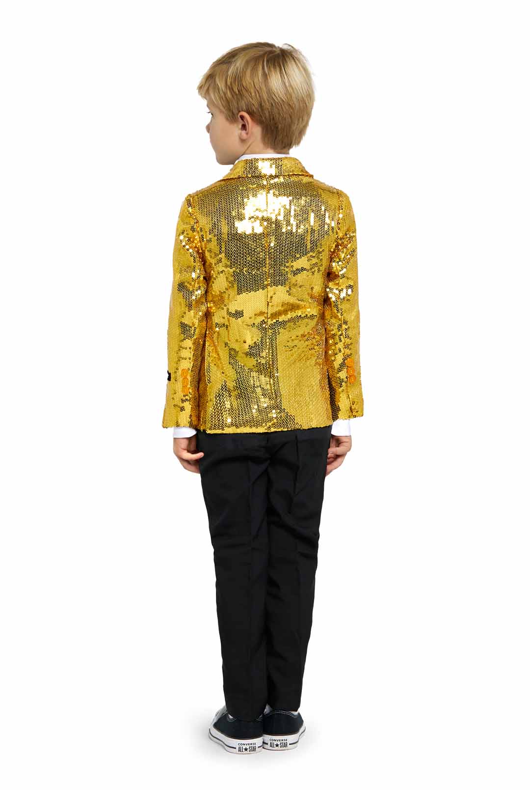 A child with blond hair is standing and facing away from the camera, clad in a Suitmeister Sequins Gold - Sequin Blazer, complemented by black pants and black shoes featuring white soles. The backdrop is a plain white.