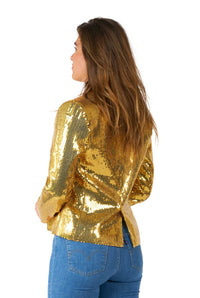 A woman with long brown hair is wearing the Sequins Gold blazer by Suitmeister paired with blue jeans. She is standing with her back to the camera, slightly turned to the side against a plain white background.