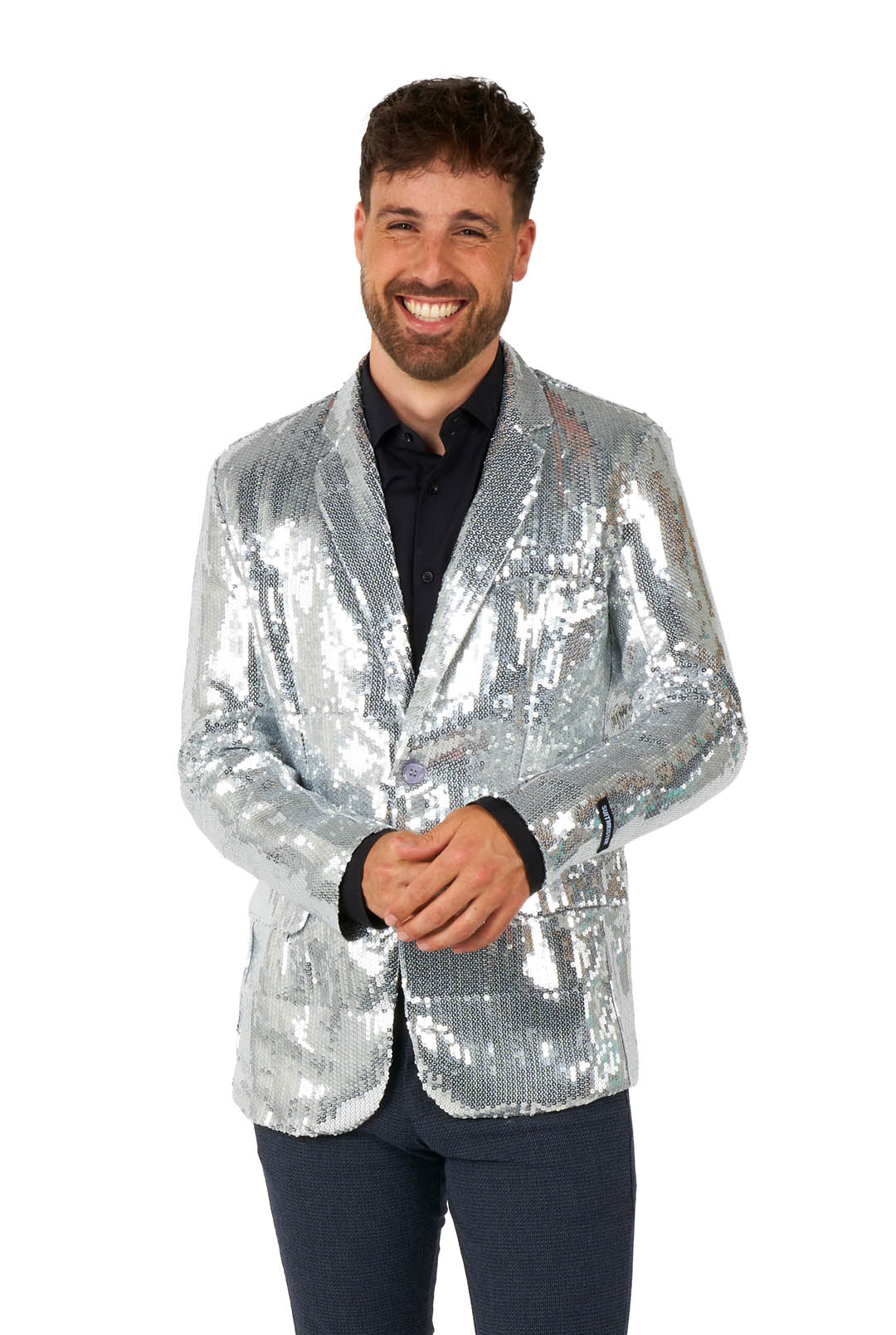 A man with short, dark hair and a beard stands against a white background, smiling and wearing the Suitmeister Sequins Blazer Silver over a black shirt, with his hands clasped in front.