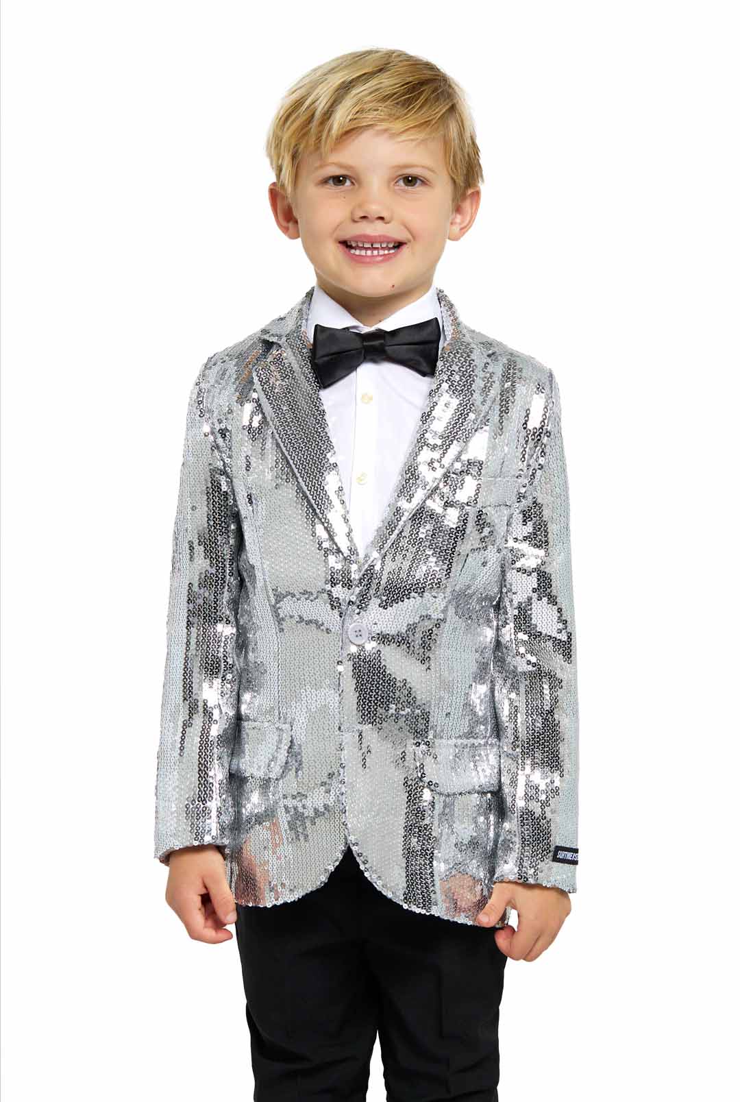 A smiling child dressed in the "Sequins Silver - Sequin Blazer" by Suitmeister, paired with a black bow tie, white shirt, and black pants, stands against a white background.