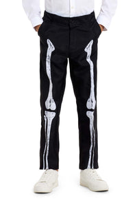 A person is dressed in Suitmeister's "Skeleton Grunge Black" pants, which feature a black base with a white skeleton bone design on the front. They are also wearing a white long-sleeve shirt and white sneakers, all set against a plain white background.