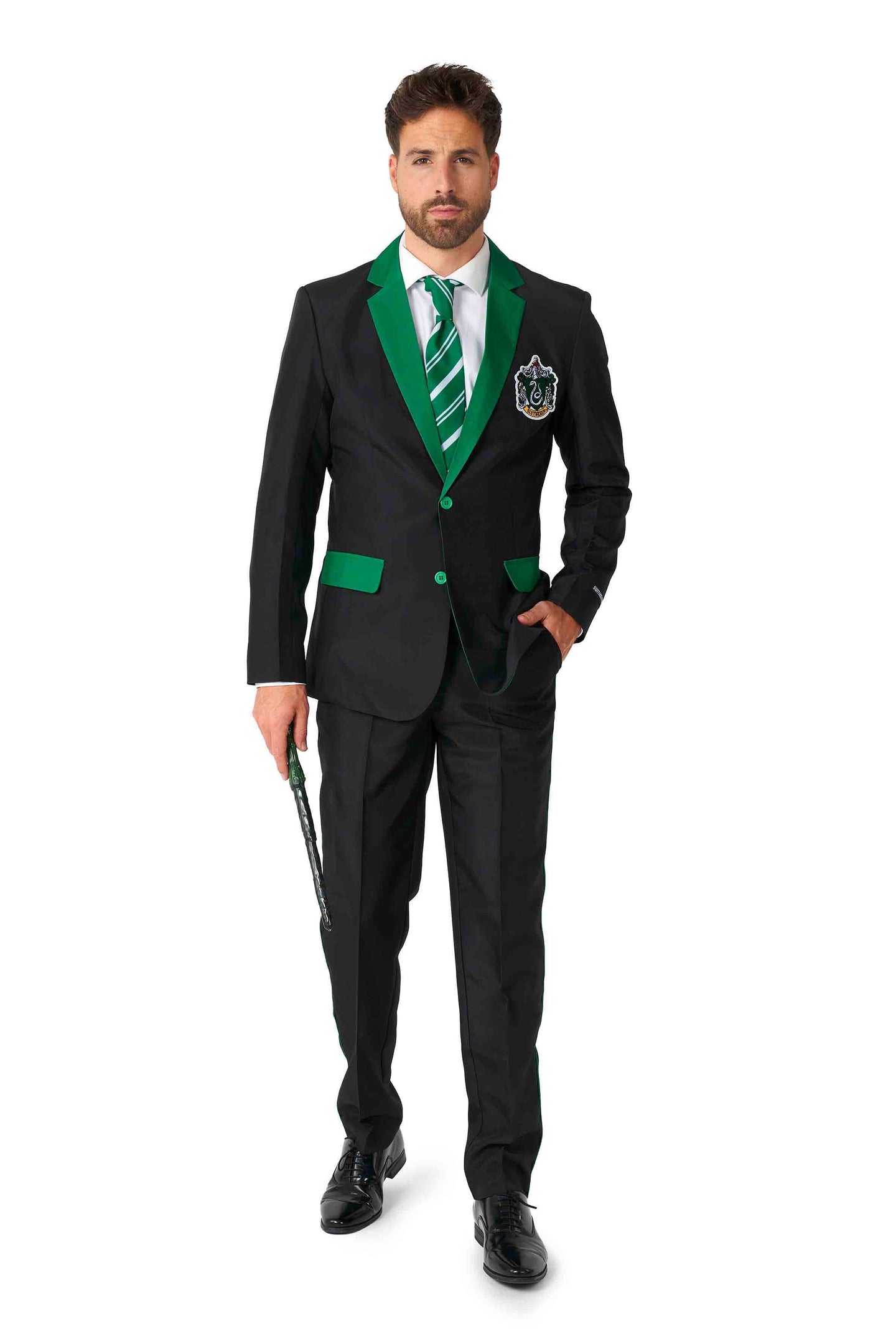 A man is dressed in the Suitmeister's Harry Potter Suit - Slytherin™, featuring a black design with green trim and a green striped tie, complete with a crest on the left chest. He holds a wand and sports short brown hair, a beard, and wears black shoes.